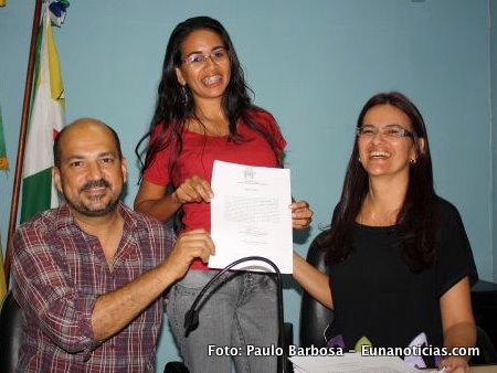 A servidora exibe o ato de posse juntamente com o prefeito Rob&eacute;rio Oliveira e a secret&aacute;ria de Sa&uacute;de Katia Nunes
