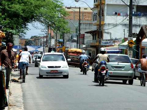 Pedestres, ciclistas, motociclistas e carros disputam o espaço entre as barracas e a pista de rolagem